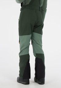 Groene en donkergroene waterdichte broek met een brede pijpdesign, voorzien van zijritsen en een gestructureerde afwerking, geschikt voor buitensporten.