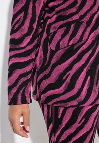Tessuto a righe zebrate nero e rosa che presenta una giacca su misura con tasca sul petto. Texture liscia, design aderente e maniche lunghe.
