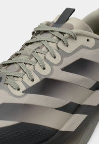 Beiger und grauer Sportschuh mit strukturiertem Obermaterial, gemusterten Überzügen, hellgrünen Schnürsenkeln und verstärkter Fersenschlaufe.