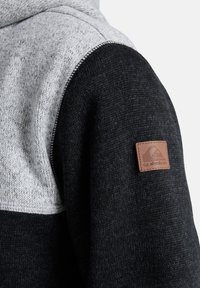 Felpa con cappuccio caratterizzata da una combinazione di tessuti a maglia grigia e nera, superficie testurizzata e una patta in pelle marrone con logo sul maniche.