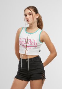 Hvit croppet tank topp med turkise detaljer, med en sentral snøring og rosa logo. Kombinert med svarte shorts som har snøring på siden.