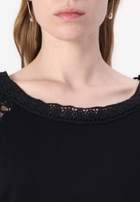 Top nero con un ampio scollo in pizzo decorato da motivi floreali. Il tessuto appare liscio e le maniche corte aggiungono un tocco delicato.