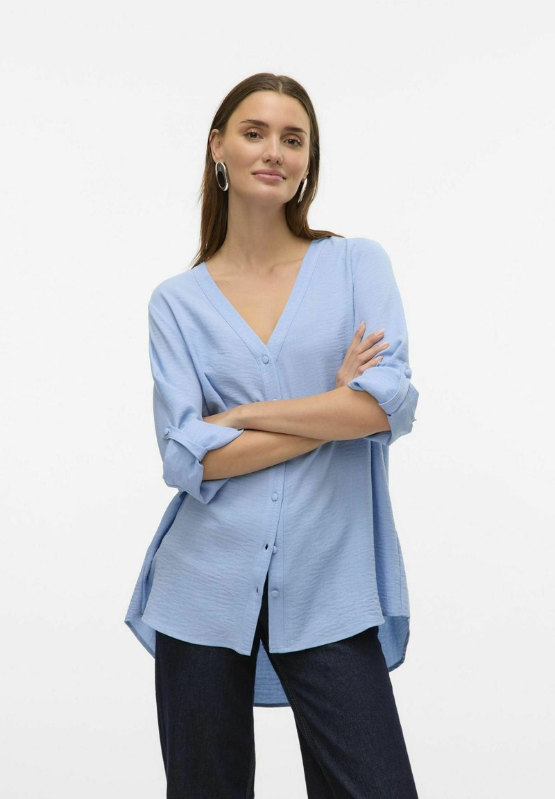 Lys blå, knap-op skjorte med v-hals og opfoldede ærmer. Har en løs pasform og struktureret stof. Bæres med mørk denim.