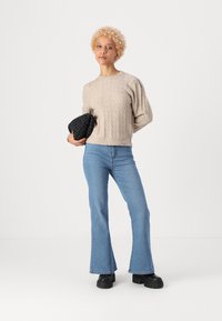 Beige knitted sweater with raised pattern, blue flared jeans, and black platform shoes. Model holding a textured black clutch.