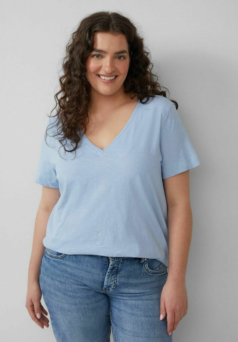 Lichtblauw katoenen T-shirt met een V-hals, korte mouwen en een relaxte pasvorm. Gecombineerd met lichte denim jeans. Glad van textuur.