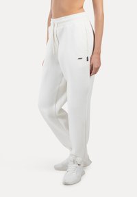 Weiße Jogginghose aus weichem Stoff mit elastischem Bund und Kordelzug. Sie verfügt über seitliche Taschen und ein kleines Logo am Oberschenkel.