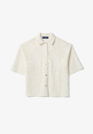 Camisa corta de manga corta color crema con patrón de encaje de ojales florales y cuello puntiagudo, corte cropped.