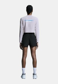 Ljusrosa långärmad topp med blå text "ON RUNNING", i kombination med svarta shorts. Modellen bär vita skor och strumpor, visad bakifrån.