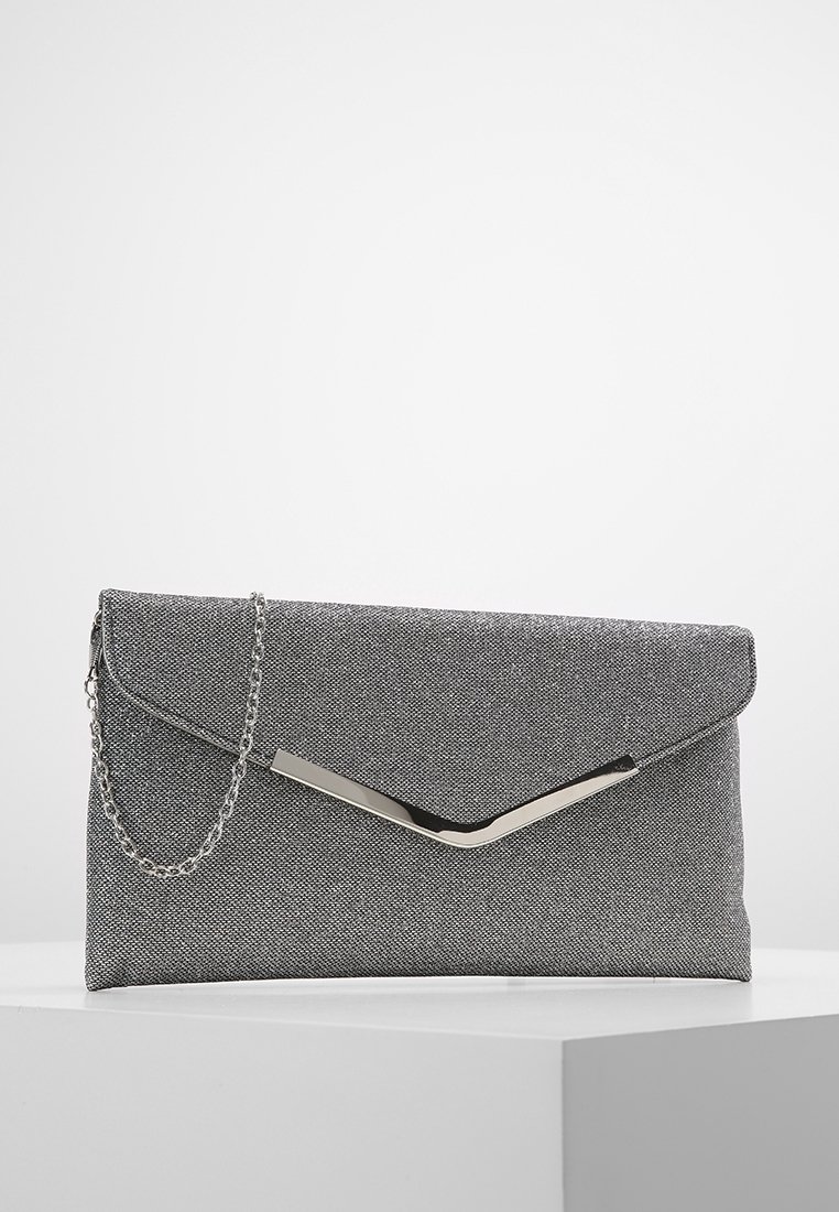 Pochette enveloppe gris texturé avec fermoir en forme de chevron argenté et bandoulière chaîne argentée amovible sur socle blanc.