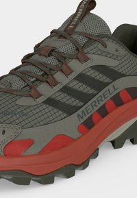 Chaussure de randonnée Merrell grise et rouge avec empeigne en mesh, lacets à motifs et semelle robuste pour une utilisation en extérieur.