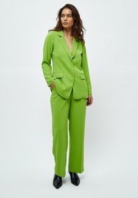 Svijetlozeleni odijelo s krojem, s sakojem na jedan gumb i hlačama širokih nogavica. Glatka tekstura i elegantan dizajn, uparen s crnim cipelama na špic.