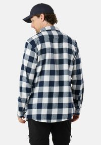 Marineblauwe en witte geblokte flanellen shirt met lange mouwen, knoopsluiting en standaard kraag, van achteraf zichtbaar, gedragen door een model met een pet.
