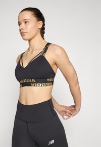 Top deportivo negro corto con logo dorado en las tiras, con un escote en V y una banda ancha, combinado con leggings negros de tiro alto.