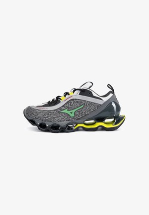 Scarpa sportiva grigia e nera con logo verde, accenti gialli, lacci neri e suola segmentata unica con sezioni cave.