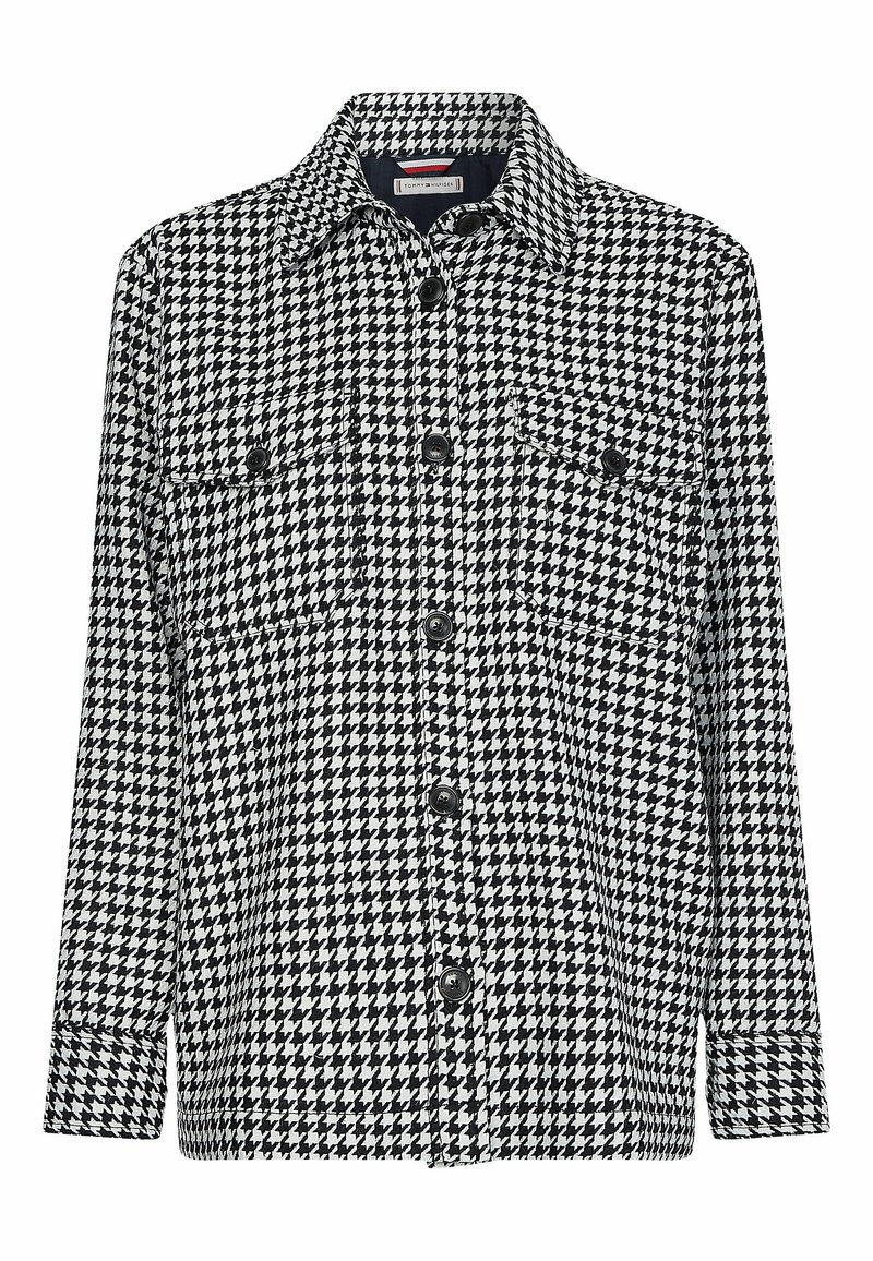 Chaqueta camisa de estampado pata de gallo en blanco y negro con cuello tipo solapa, cierre delantero de botones y dos bolsillos en el pecho. Textura suave.