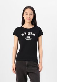 Melna kokvilnas T-kreklu ar īsām piedurknēm un apaļu dekoltē. Priekšpusē ir balta grafiska printa uzraksts "JAUNĀ DENIM KLUBS".