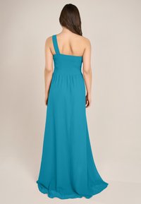 Türkises, einseitiges Maxikleid mit einem gerüschten Oberteil, fließendem Rock und weichem Stoff. Der Rücken ist offen und betont eine entspannte Silhouette.