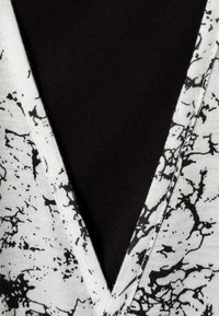Top con scollatura a V in tessuto bianco con motivo marmorizzato nero, contrastato da uno sfondo nero solido e texturizzato.