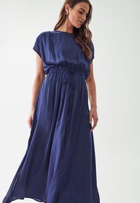 Navy blue, polvasta pituinen mekko, jossa on lyhyet hihat, vyötäröä korostava leikkaus ja virtaava hame. Valmistettu kevyestä, sileästä kankaasta.