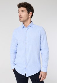 Camicia azzurra a maniche lunghe in tessuto testurizzato con colletto a punta, caratterizzata da bottoni chiari e orlo curvo.