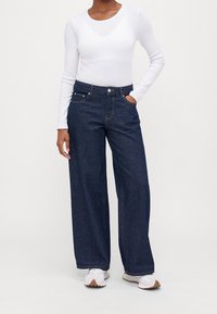 Breda denimjeans i mörknyans med synlig sömnad, framfickor och hög midja, kombinerat med en figurn snug vit långärmad topp.