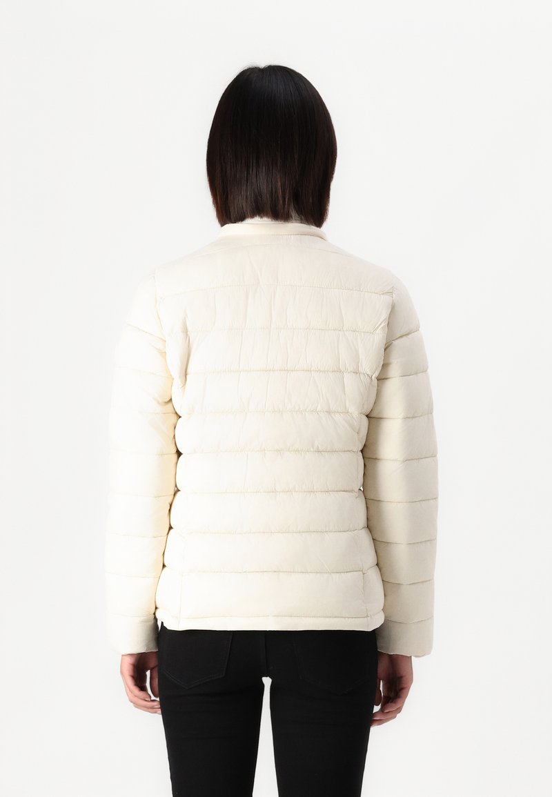 Giacca puffer beige chiaro con motivo trapuntato orizzontale, colletto alto e maniche lunghe, indossata sopra pantaloni neri. Vista posteriore mostrata.