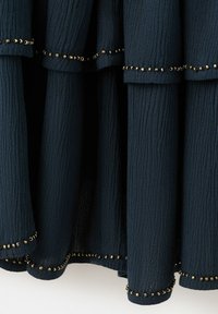 Ciemna tkanina o fakturze z pionowymi fałdami, każdy brzeg ozdobiony jest małymi metalicznymi złotymi koralikami wzdłuż brzegu i szwów.