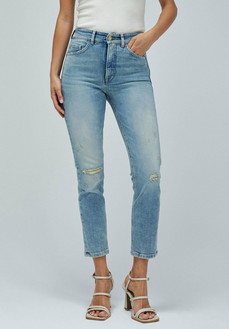 Jeans de denim azul claro con cintura alta, detalles desgastados y perneras cortas. Cuentan con cinco bolsillos y un cierre de botón. Tejido texturizado.