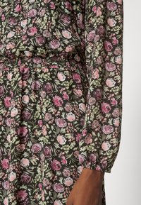 Kukkakuvioinen mekko mustalla pohjalla, jossa on pinkkejä ja vihreitä ruusukuvioita, vyötärö kootulla vyötäröllä ja joustavat hihat. Kevyt kangas.