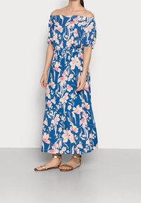 Robe maxi bleue à épaules dénudées avec un motif floral en rose et blanc, taille élastique, manches courtes et silhouette fluide.
