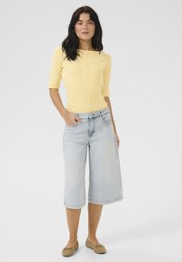 Gul ribbet top med rund halsudskæring og korte ærmer, sat sammen med lyseblå wide-leg denim culotter. Beige flade sko fuldender looket.