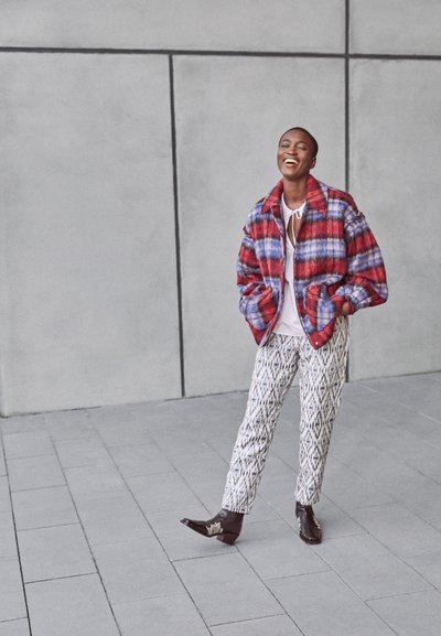 Casaco oversized em padrão xadrez vermelho e azul, parte de cima branca, calças brancas estampadas e botas pretas de bico fino; silhueta estruturada com textura suave.