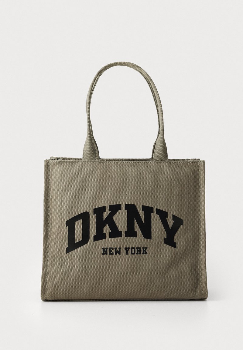 Sac en toile beige avec le logo noir "DKNY NEW YORK". Dispose de deux poignées solides et d'une fermeture zippée sur le dessus.