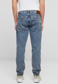 Blugi din denim albastru estompat, cu un design drept, având două buzunare pe spate și o etichetă din piele pe talie.