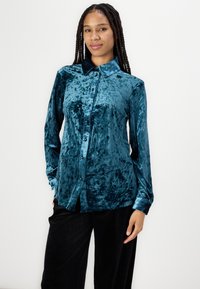 Teal velvet shirt with a collared neck, long sleeves, and front button closure. Soft texture with a slightly shiny finish.