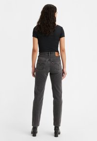 Top negro de canalé combinado con jeans de tiro alto en gris oscuro, que incluyen una parche de cuero, bolsillos traseros curvados y diseño de pierna recta.