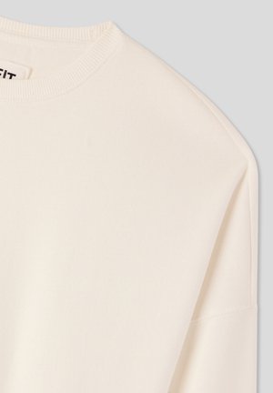 Kremowy sweatshirt z okrągłym dekoltem, miękką fakturą i opadającymi szwami na ramionach. Materiał wydaje się gładki i lekki.