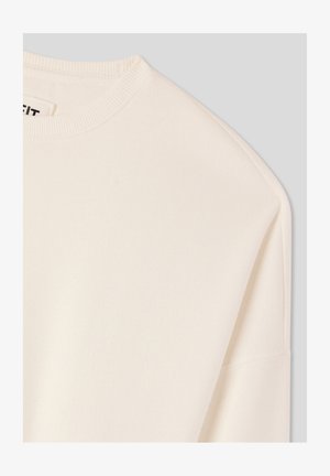 Kremowy sweatshirt z okrągłym dekoltem, miękką fakturą i opadającymi szwami na ramionach. Materiał wydaje się gładki i lekki.