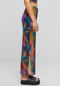 Pantaloni ampi e trasparenti di colori diversi con motivi astratti in viola, blu, verde e arancione. Presentano fessure laterali e una texture liscia.