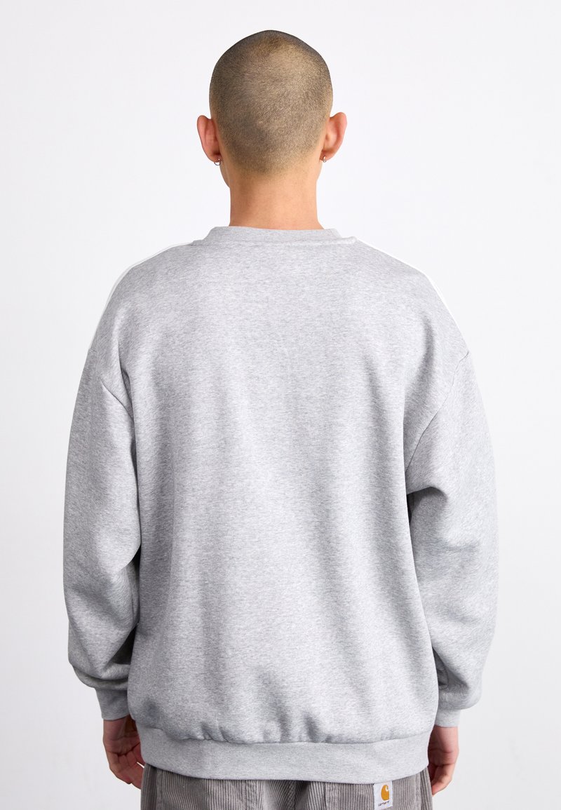 Sweat-shirt gris à col rond, coupe ample, avec des poignets et un ourlet côtelés, fabriqué en tissu doux. Présente une étiquette de logo sur le côté.