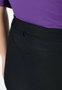 Czarne legginsy z wysokim stanem o teksturowanym wykończeniu, z małą kieszonką na zamek na pasku. Materiał wydaje się elastyczny.