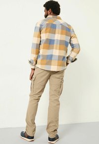 Langärmliges, karierter Hemd in beige, blau und senfgelben Tönen; kombiniert mit beigen Cargo-Hosen mit seitlichen Taschen und einer lässigen Passform.