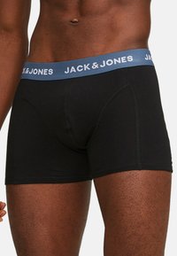Schwarze Baumwollboxershorts mit einem blauen elastischen Bund, der mit dem weißen Text "JACK & JONES" versehen ist. Glatte Textur, enganliegenden Schnitt und Standardlänge.