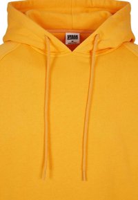 Sudadera amarilla con capucha ajustable, hecha de tela suave. Presenta un bolsillo canguro y puños de canalé. La etiqueta dice "URBAN CLASSICS."