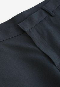 Schwarze Stoffhosen mit strukturiertem Finish, flacher Vorderseite, Gürtelschlaufen und traditionellem Bund für einen festen Look.