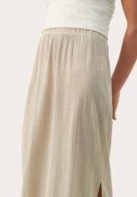 Jupe plissée beige avec une taille élastique, ornée de rayures texturées et d'une fente latérale. Le tissu a un éclat subtil.