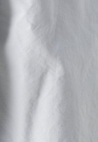 Valkoinen kangas, jossa on hieman ryppyinen rakenne. Materiaali vaikuttaa kevyeltä ja sileältä, ja siinä on pehmeitä poimuja sekä kevyitä heijastuksia.