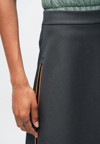 Fekete szoknya sima textúrával, oldalzippzárral, narancssárga, piros és sárga kiegészítőkkel. Az anyag könnyűnek és testhezállónak tűnik.