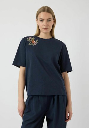 Marineblå bomulds T-shirt med korte ærmer og rund halsudskæring, med farverig blomsterbroderi på venstre skulder.
