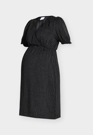 Fekete midi ruha fehér pöttyökkel, fodros rövid ujjak, rugalmas derék és V-nyak egy egyszerű világos háttéren.